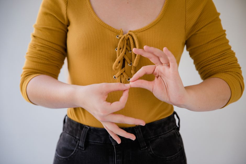 A person signing "wish" or "desire" in Mexican Sign Language (LSM), showing the handshape near the chest with a hopeful facial expression.